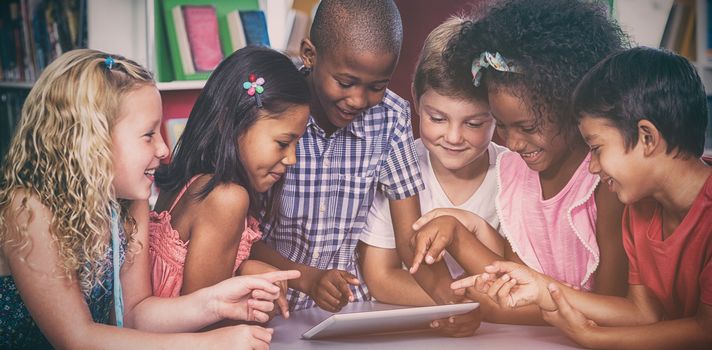 Happy multi ethnic children using digital table in library 