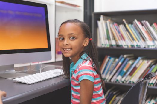 Portrait of happy African-american schoolgirl sitting and looking at camera  in computer room 