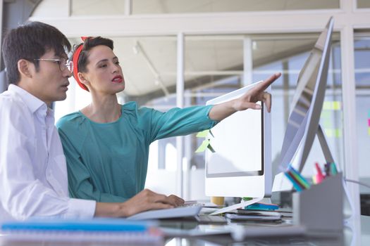 Side view of business people discussing over computer at desk in office