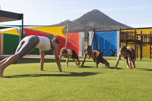 Front view of caucasian trainer teaching yoga to students on grass in school playground at schoolyard