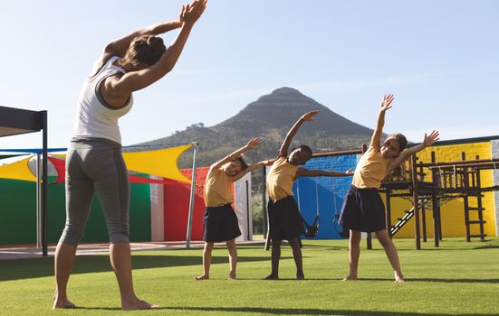 Trainer teaching yoga to students in school playground at schoolyard