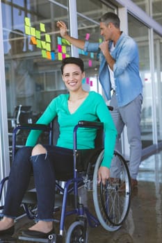 Disabled businesswoman looking at camera while male executive writing on sticky notes in office