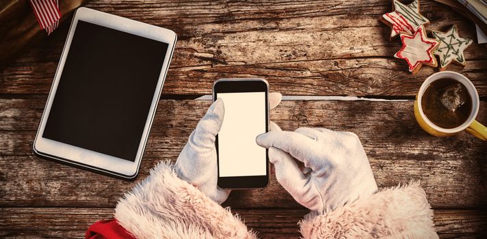 Cropped image of santa claus using mobile phone with Christmas cookies and cup of coffee on wooden table