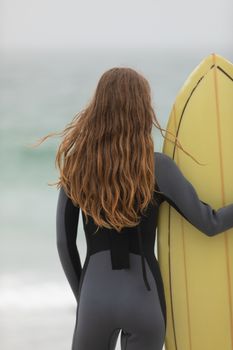 Rear view of caucasian female surfer standing with surfboard on the beach