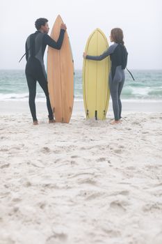 Rear view of young multi-ethnic couple surfer holding surfboards on the beach