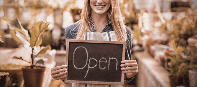 Portrait of young woman holding open sign placard at greenhouse