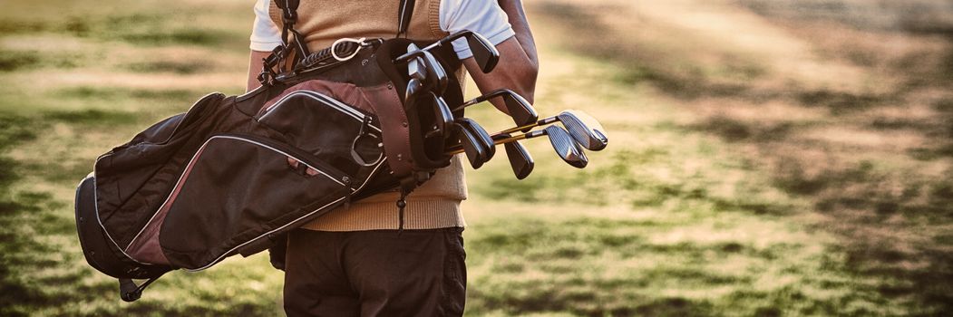 Man carrying golf bag while standing on field, Rear view