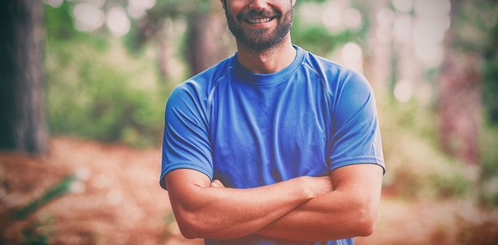 Portrait of smiling man standing in forest with arms crossed