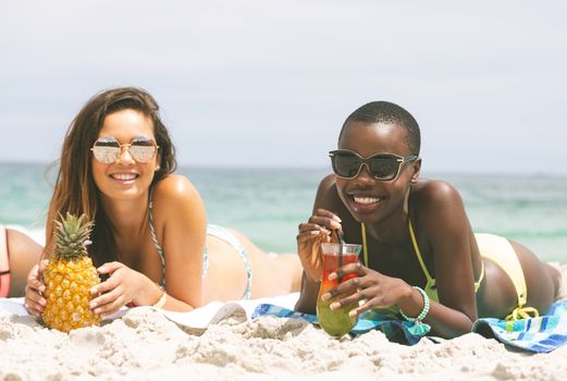 Front view of multi ethnic women lying at beach while having pineapple on sunny day