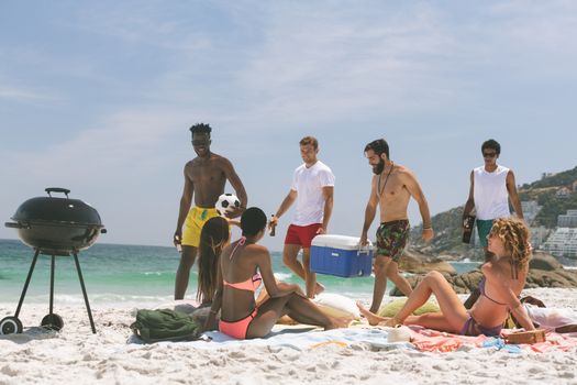 Front view of multi ethnic group of friends relaxing and enjoying at beach on a sunny day. Preparing barbecue