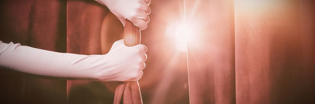 Cropped hands in white gloves holding curtain at illuminated stage