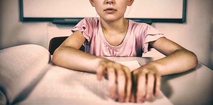 Schoolgirl reading a braille book in classroom at school