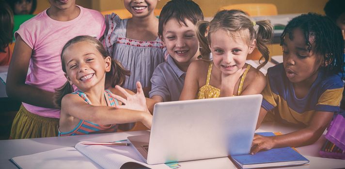 Portrait of smiling multi ethnic children using laptop in clasroom
