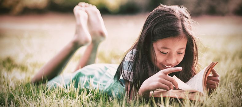 Smiling girl lying on grass and reading book in park on a sunny day