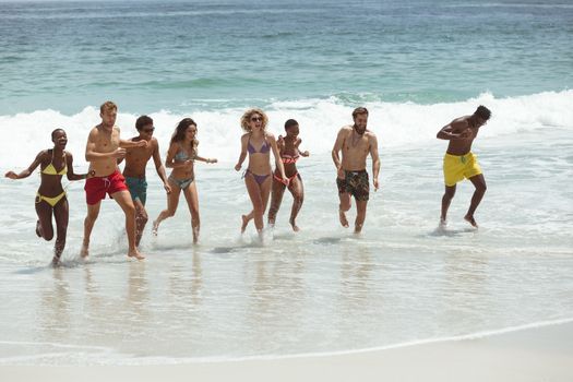 Front view of multi ethnic group of friends enjoying and runing on sea  at beach on sunny day
