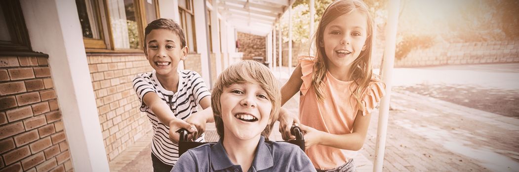 Portrait of school kids pushing a boy on wheelchair in school corridor