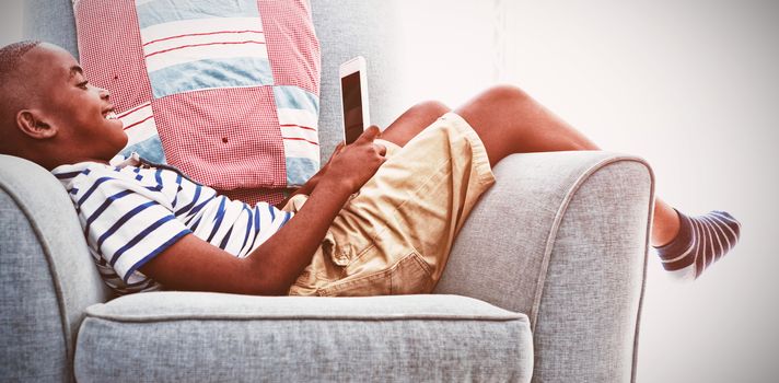 Side view of smiling boy looking at mobile phone while lying on armchair in sitting room