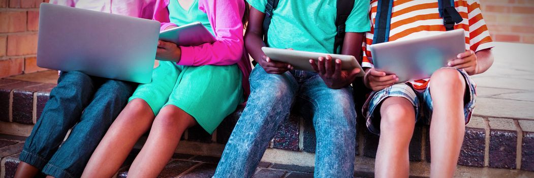 Kids sitting on staircase using laptop and digital tablet at school