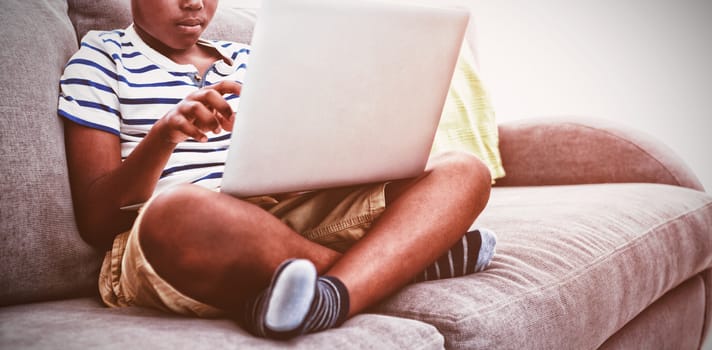 Boy using laptop while sitting with crossed legged on sofa in living room at home