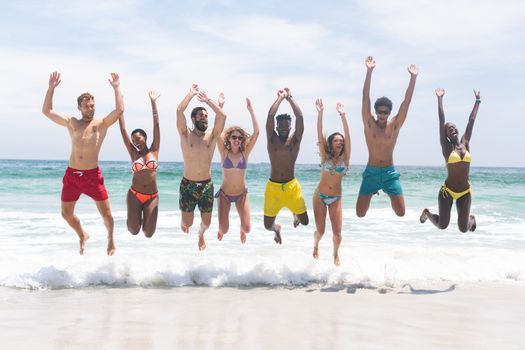 Front view of multi-ethnic group of friends relaxing  and jumping in water at beach on a sunny day