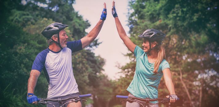 Happy athletic couple giving high five while riding bicycle on the road