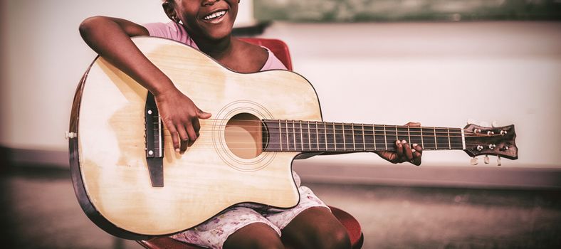Portrait of smiling schoolgirl playing guitar in classroom at school