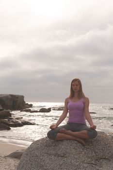 Front view of Caucasian blonde woman perform yoga on the beach. She is relaxed