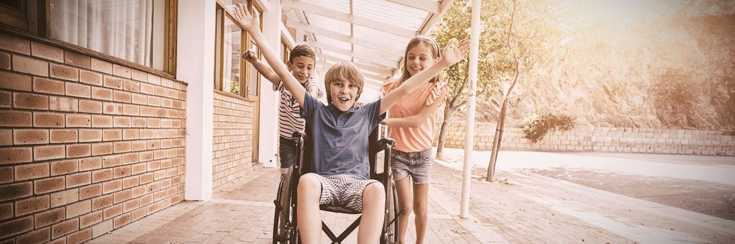 Happy school kids pushing a boy on wheelchair in school corridor