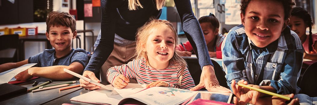 Teacher helping schoolkids with their homework in classroom at school