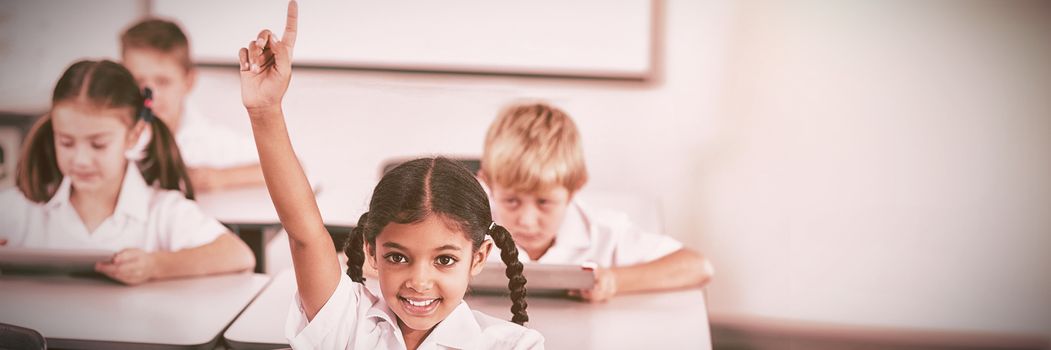 Smiling schoolgirl raising hand in classroom at school