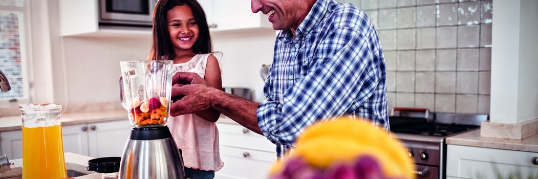 Father and daughter preparing smoothie in kitchen at home