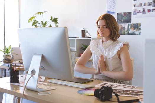 Front view of graphic designer with hand clasped doing yoga in creative office