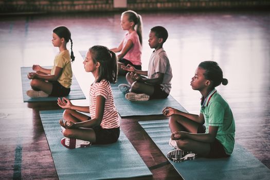 School kids meditating during yoga class in basketball court at school gym