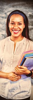 Portrait of smiling school teacher holding books in classroom at school