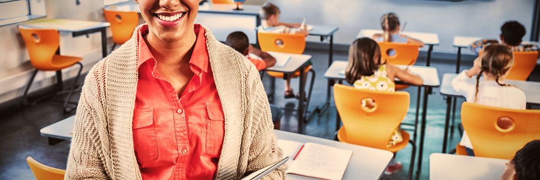 Portrait of smiling teacher standing with digital tablet in classroom