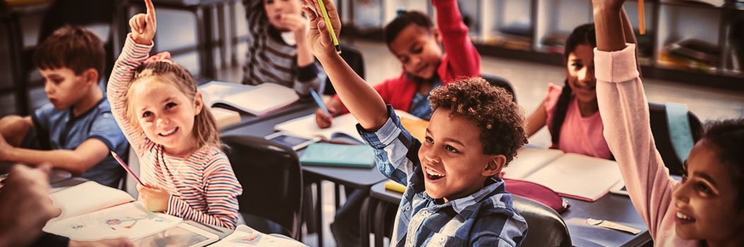 Schoolkids raising their hands in classroom at school