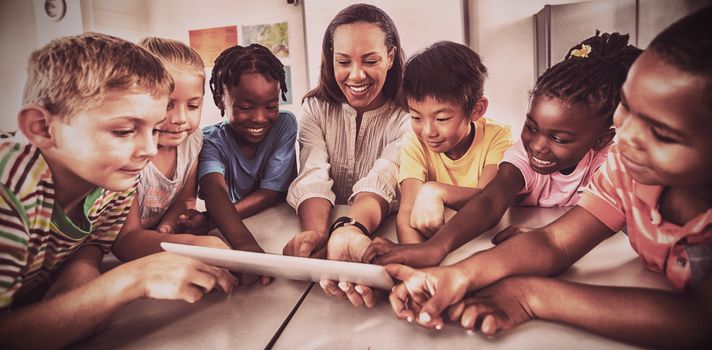 Smiling students and teacher using a tablet computer in classroom