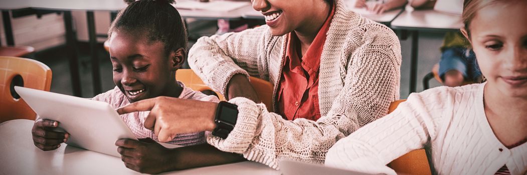 Smiling teacher helping student with tablet computer in classroom at school