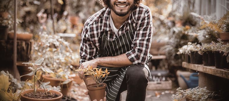 Portrait of smiling male gardener holding potted plant while kneeling outside greenhouse