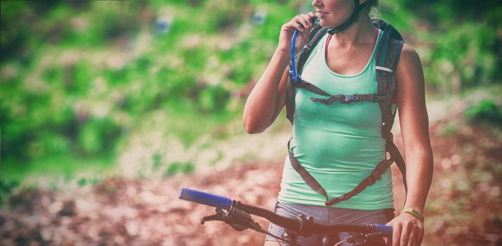 Female athletic drinking water from hydration pack in forest