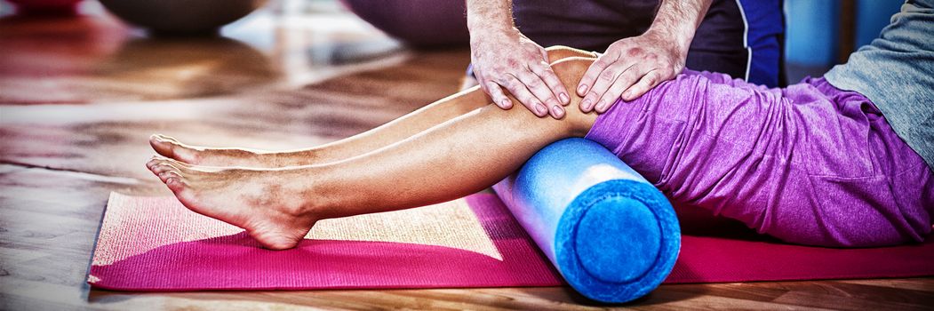 Midsection of physiotherapist assisting woman while exercising on exercise mat in clinic