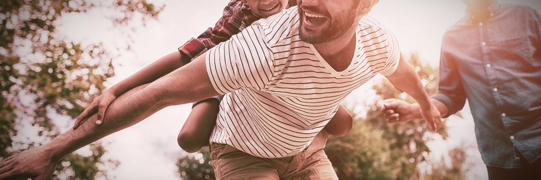 Happy grandfather looking at man giving piggy backing to son with arms outstretched in yard