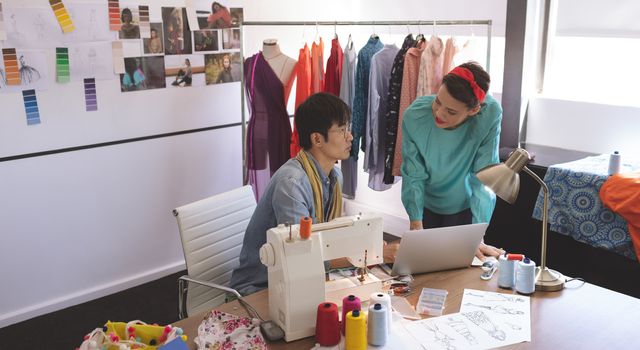 Front view of fashion designers discussing over laptop at desk in design studio 