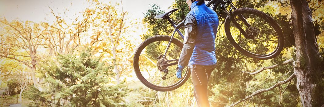 Male mountain biker carrying bicycle looking at nature in the forest