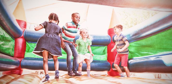 Full length of friends playing on bouncy castle at playground