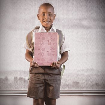 Happy schoolkid holding books and standing in classroom at school