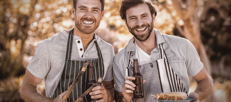 Portrait of two happy men holding barbecue meal and beer bottle in park