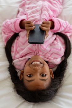 High angle view of African american girl using mobile phone while lying on bed in bedroom at home