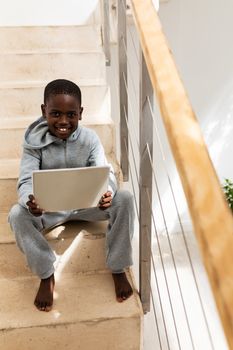 Front view of African american boy using digital tablet on staircase at home