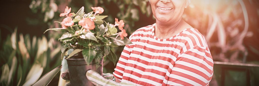Portrait of smiling woman holding potted plant while kneeling in yard